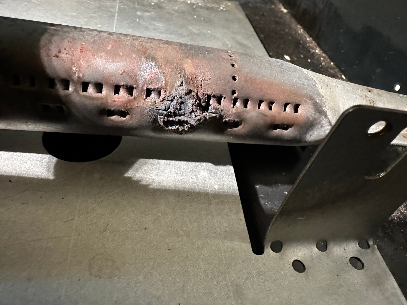 Close-up of the old American Range bake burner tube, corroded and burned through next to its flame ports