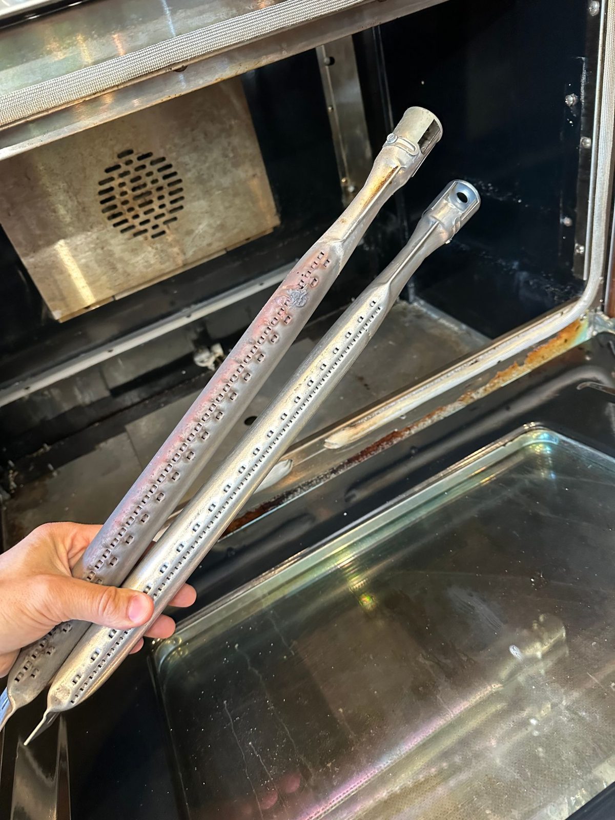 Old American Range bake burner with a burned-through spot held next to the new bake burner