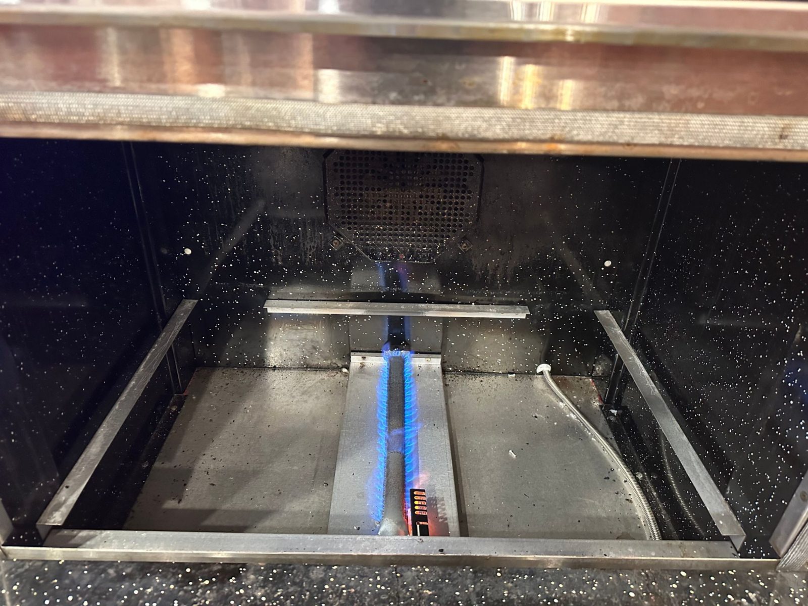 BlueStar oven with the floor panel removed, showing the bake burner lit with a blue flame and the glowing igniter at its front end