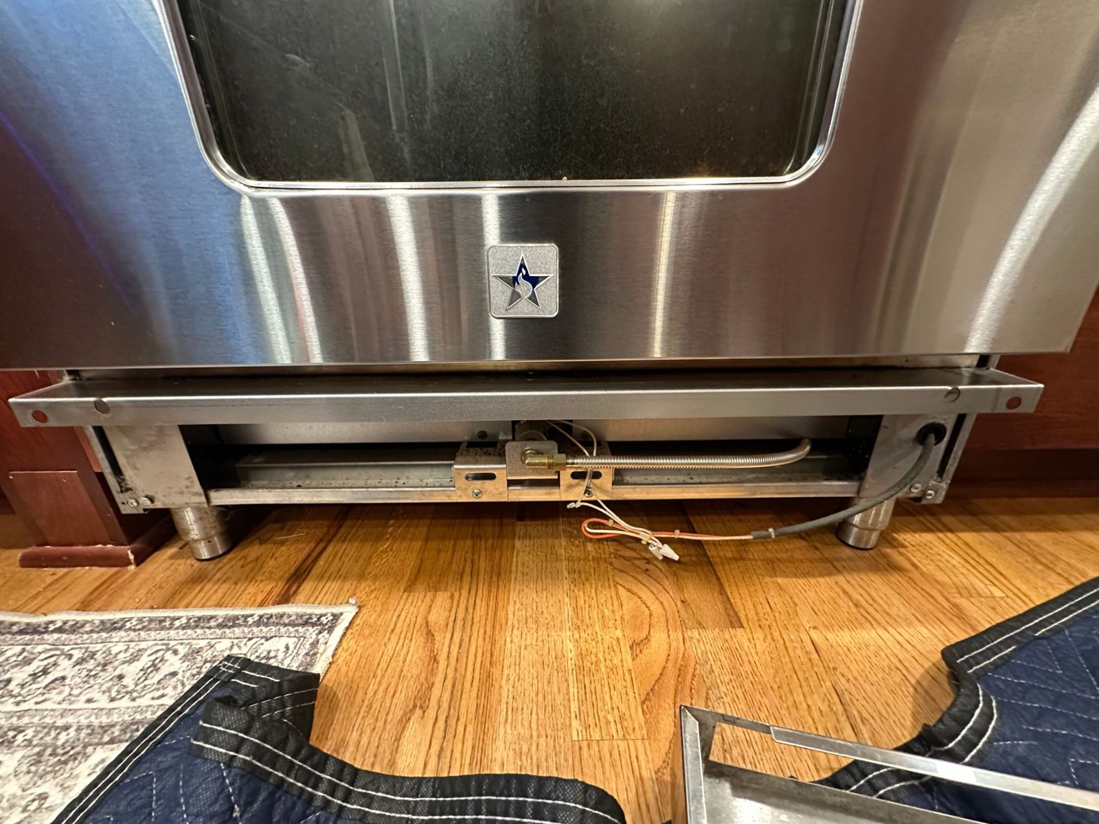 BlueStar range with the lower kick panel removed below the oven door, showing the oven gas line and igniter wiring
