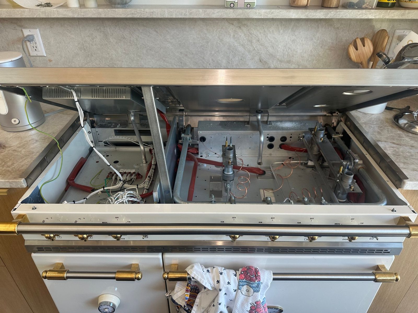 Lacanche Saulieu range in Kenmore with the cooktop lifted, exposing the induction section wiring on the left and the gas burner assemblies on the right