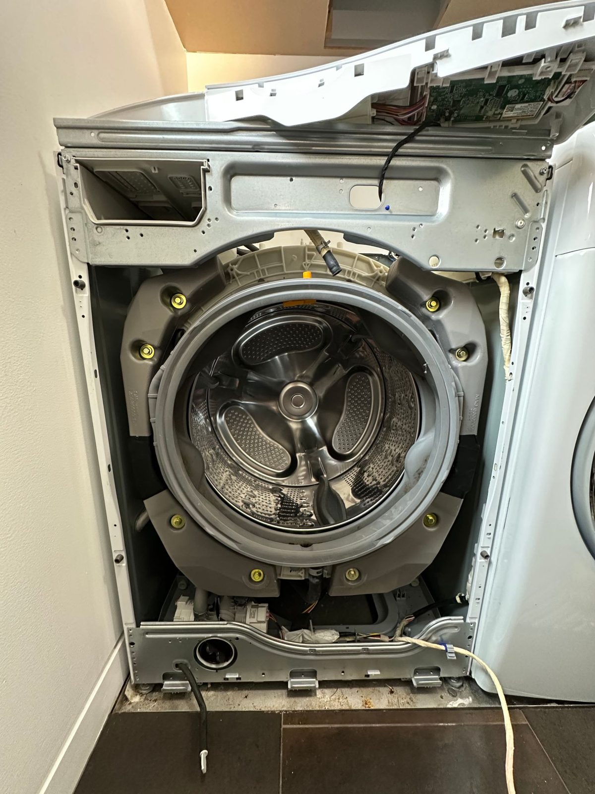 LG front-load washer with the front panel removed, the old door boot gasket still on the tub, with dark staining in its lower folds
