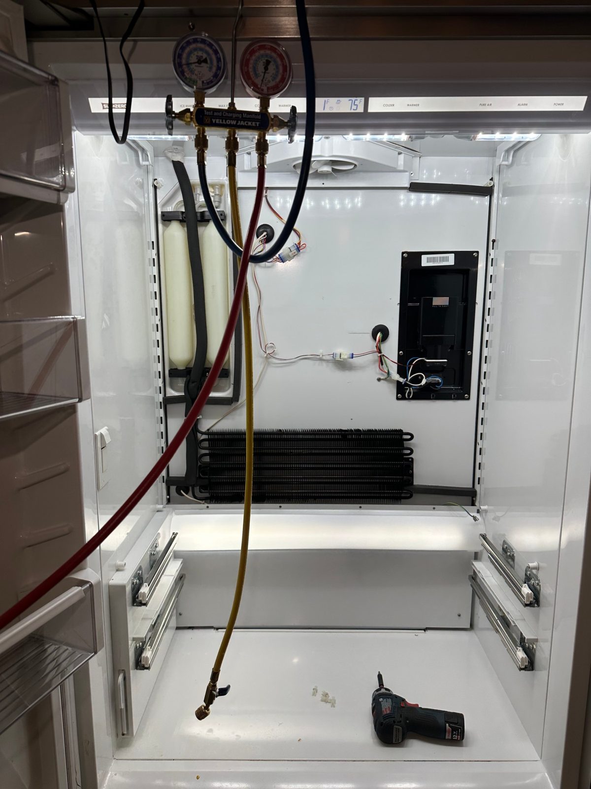 Sub-Zero refrigerator powered back on with lights on and a refrigeration gauge manifold hanging in front of the new evaporator