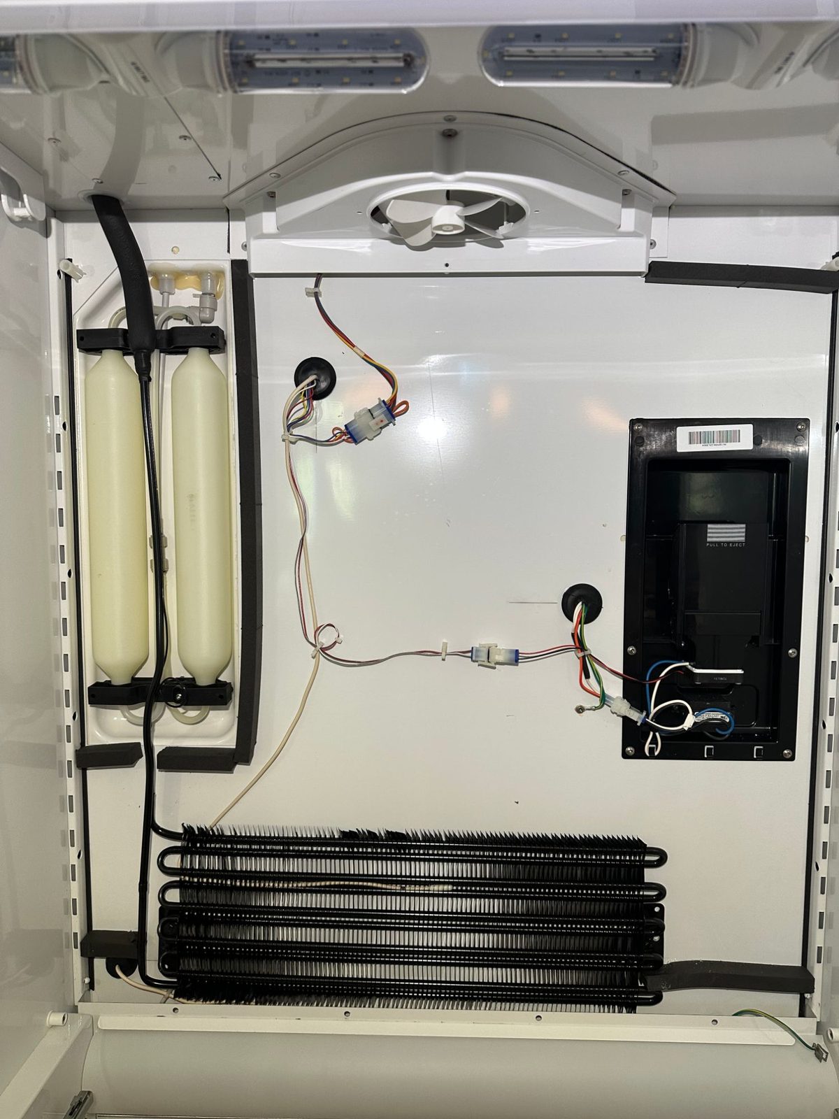 New Sub-Zero refrigerator evaporator coil mounted low on the back wall, with the fan housing and wiring above it