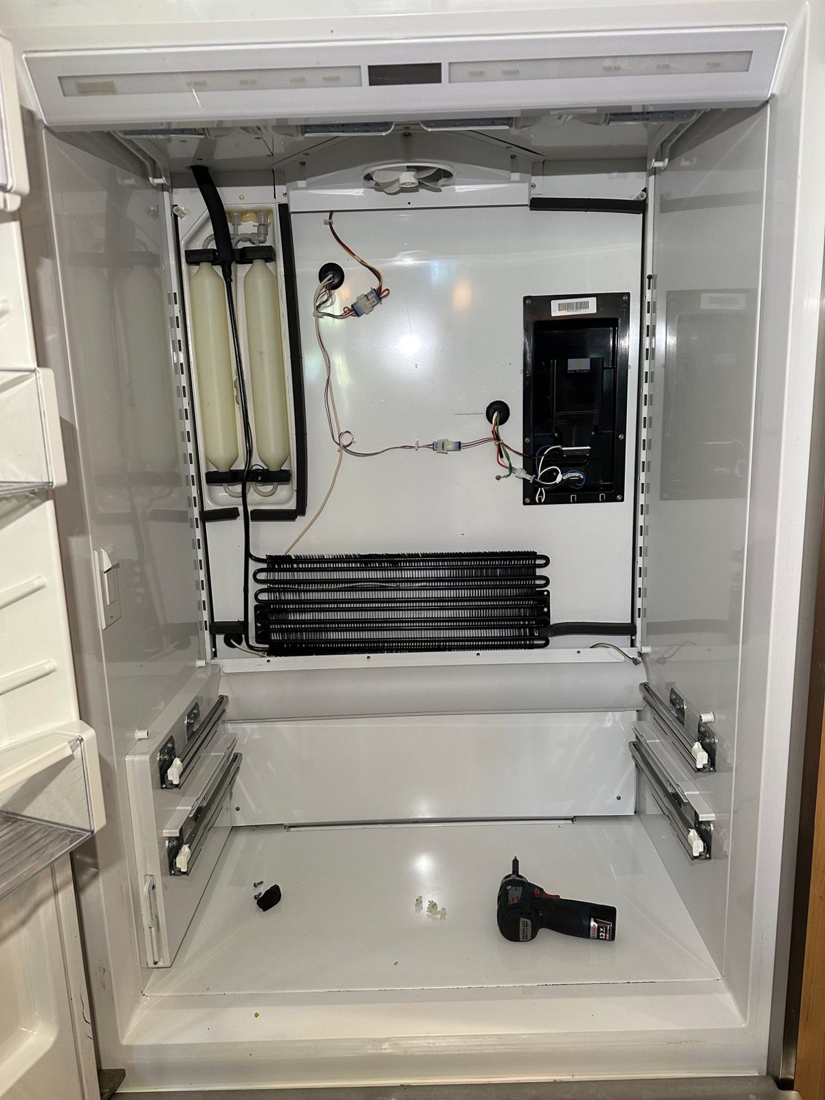 Sub-Zero refrigerator section emptied of shelves and drawers, showing the evaporator coil, fan, and water tanks on the back wall
