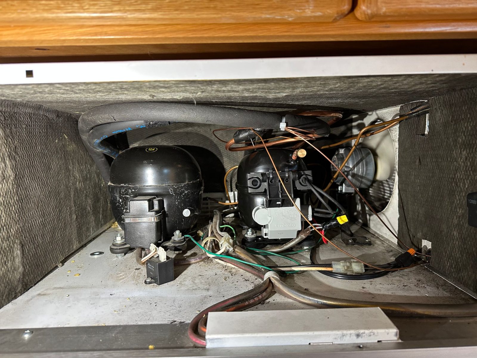 Machine compartment above the Sub-Zero 550 with its two compressors, including the new refrigerator compressor beside the freezer system's compressor, and the condenser fan