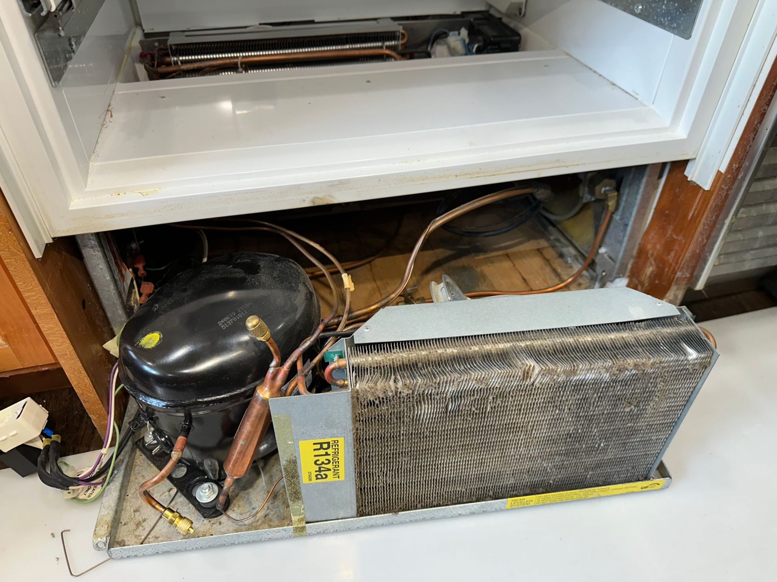 New compressor with access ports installed on the Sub-Zero machine tray next to the condenser marked R134a