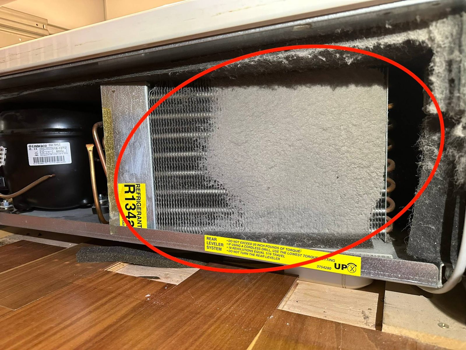 Sub-Zero 736TCI condenser coil behind the bottom grille, matted over with gray dust and lint, circled in red