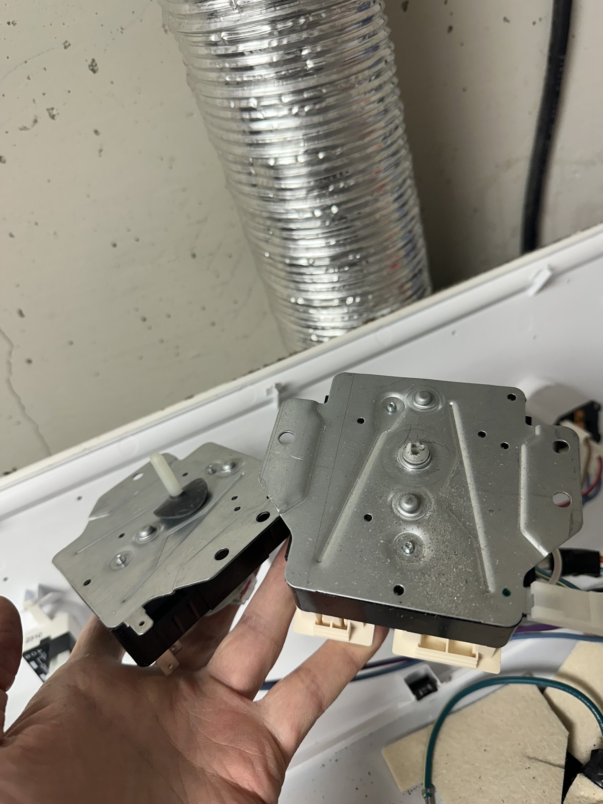 Failed appliance timer assembly removed and held next to the replacement part
