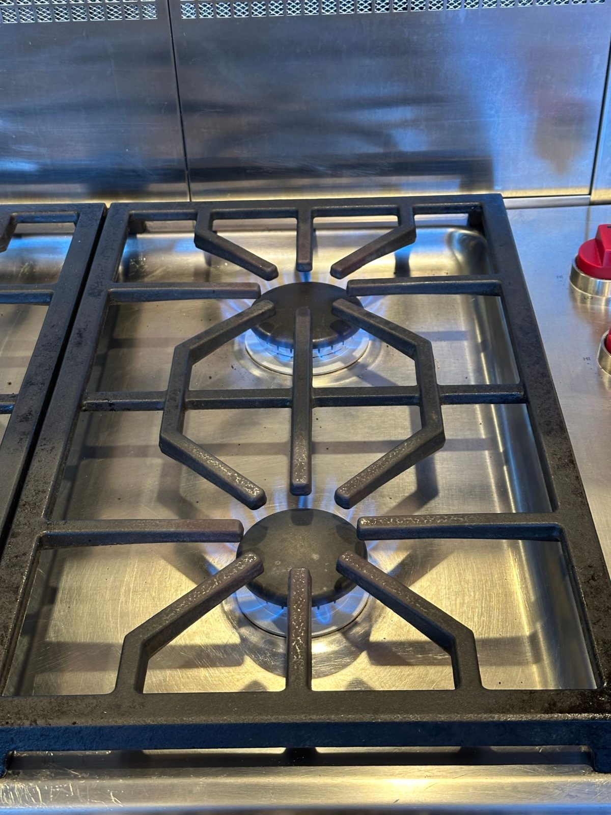 Close-up flame check on both repaired Wolf burners under the cast iron grate, even blue flame around each burner