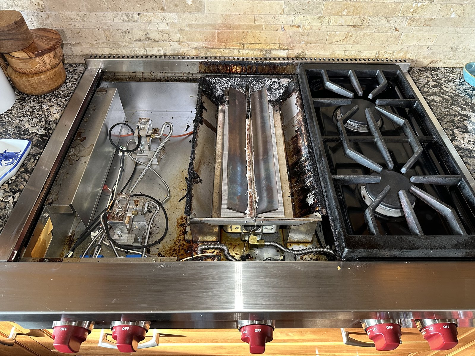 Wolf gas rangetop with center griddle burner removed, exposing burner tubes and igniter wiring during diagnosis