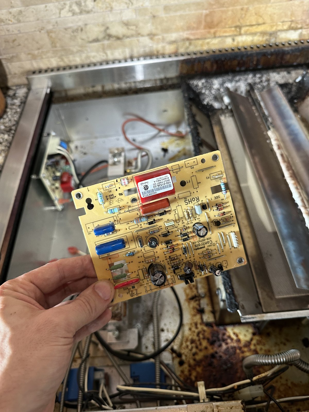 Wolf spark ignition module circuit board held up next to the open rangetop during replacement