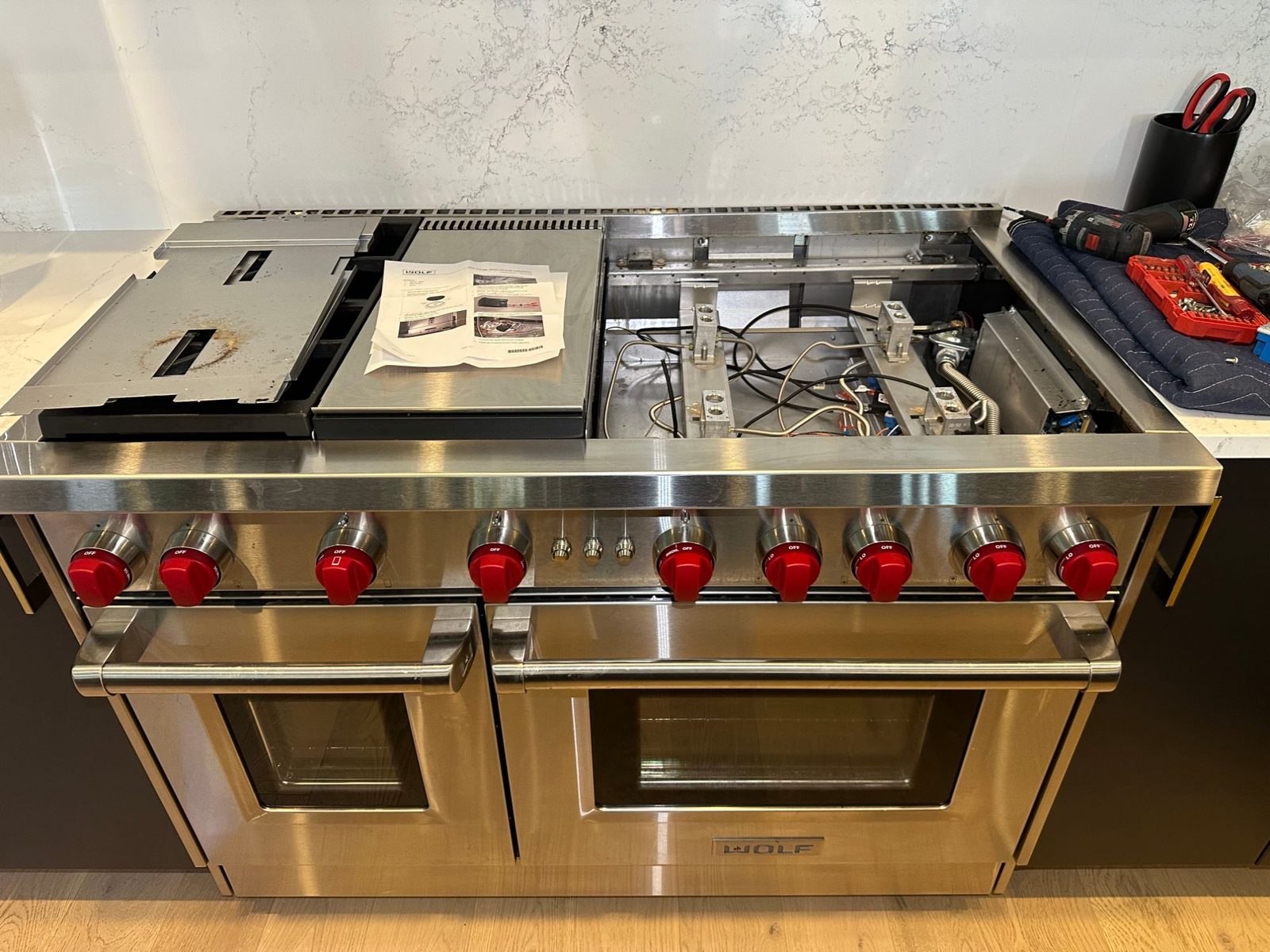 Wolf range with the right-side burner pan removed, exposing the burner bases and wiring, with the Wolf spark module instructions on the griddle